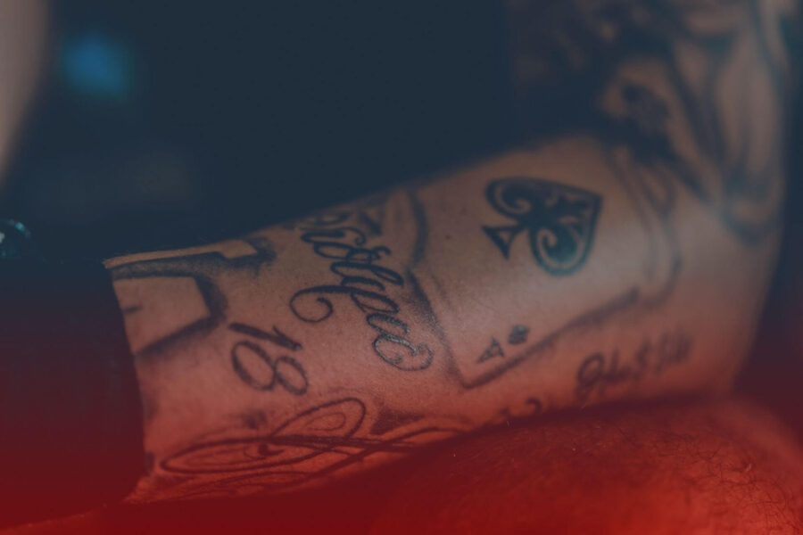 Avambraccio con tatuaggi neri di carte da gioco e scritte in corsivo, in primo piano